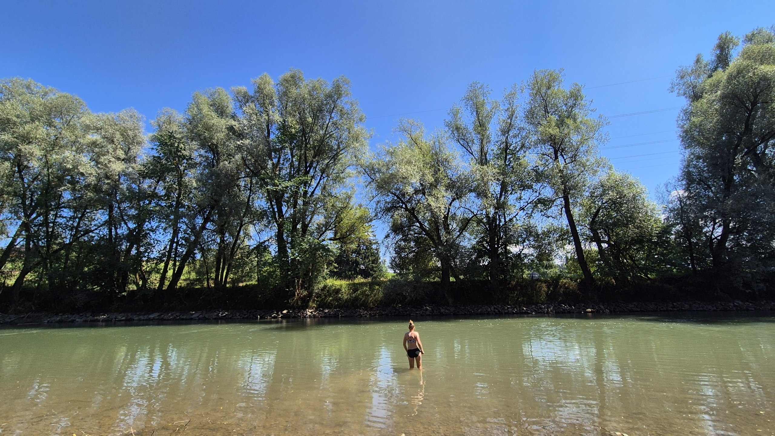Caro wading into the cold River Iller beneath the trees