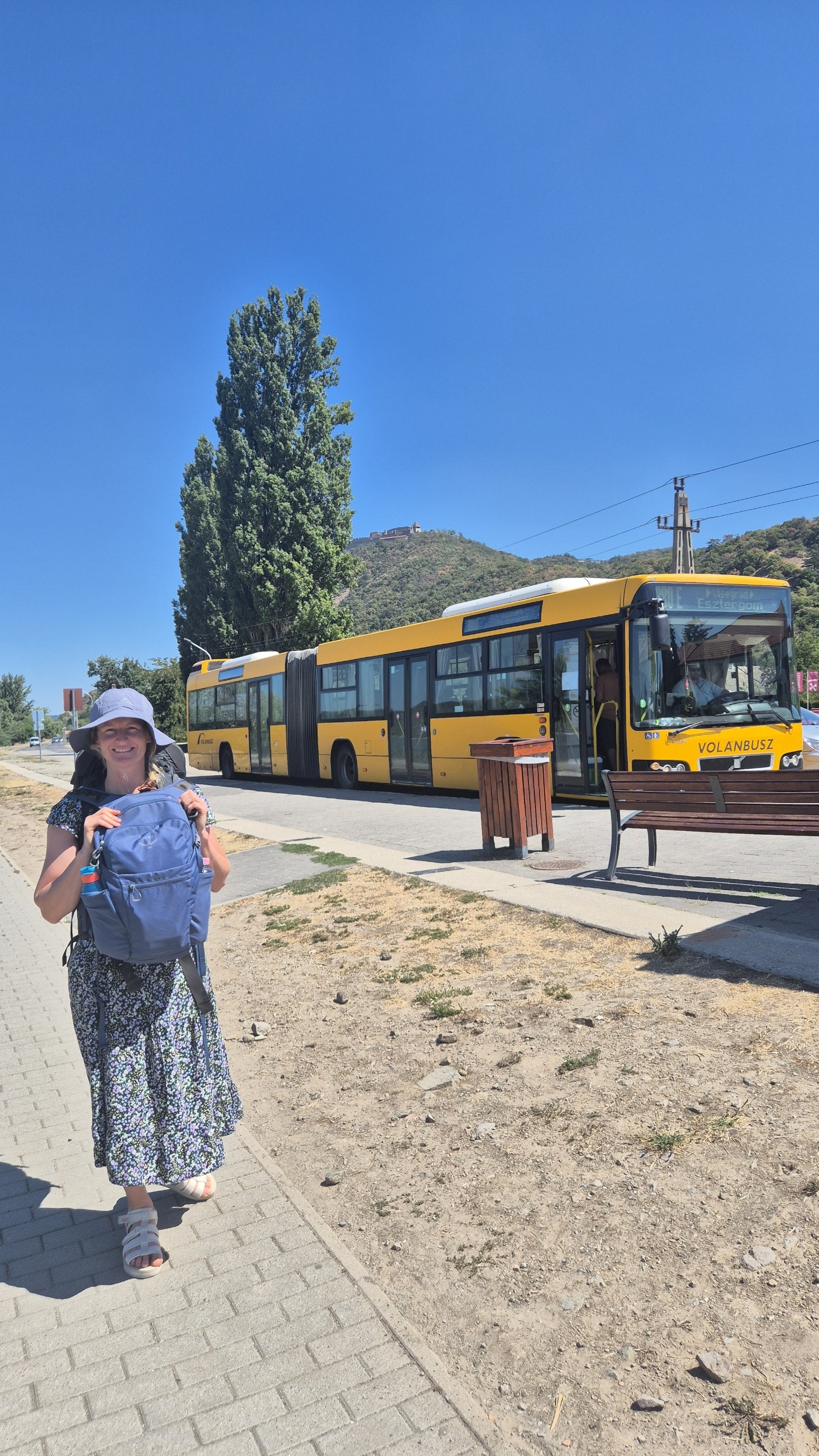 Caro beside the yellow bus after arriving in Visegrád, with the citadel on the hill
