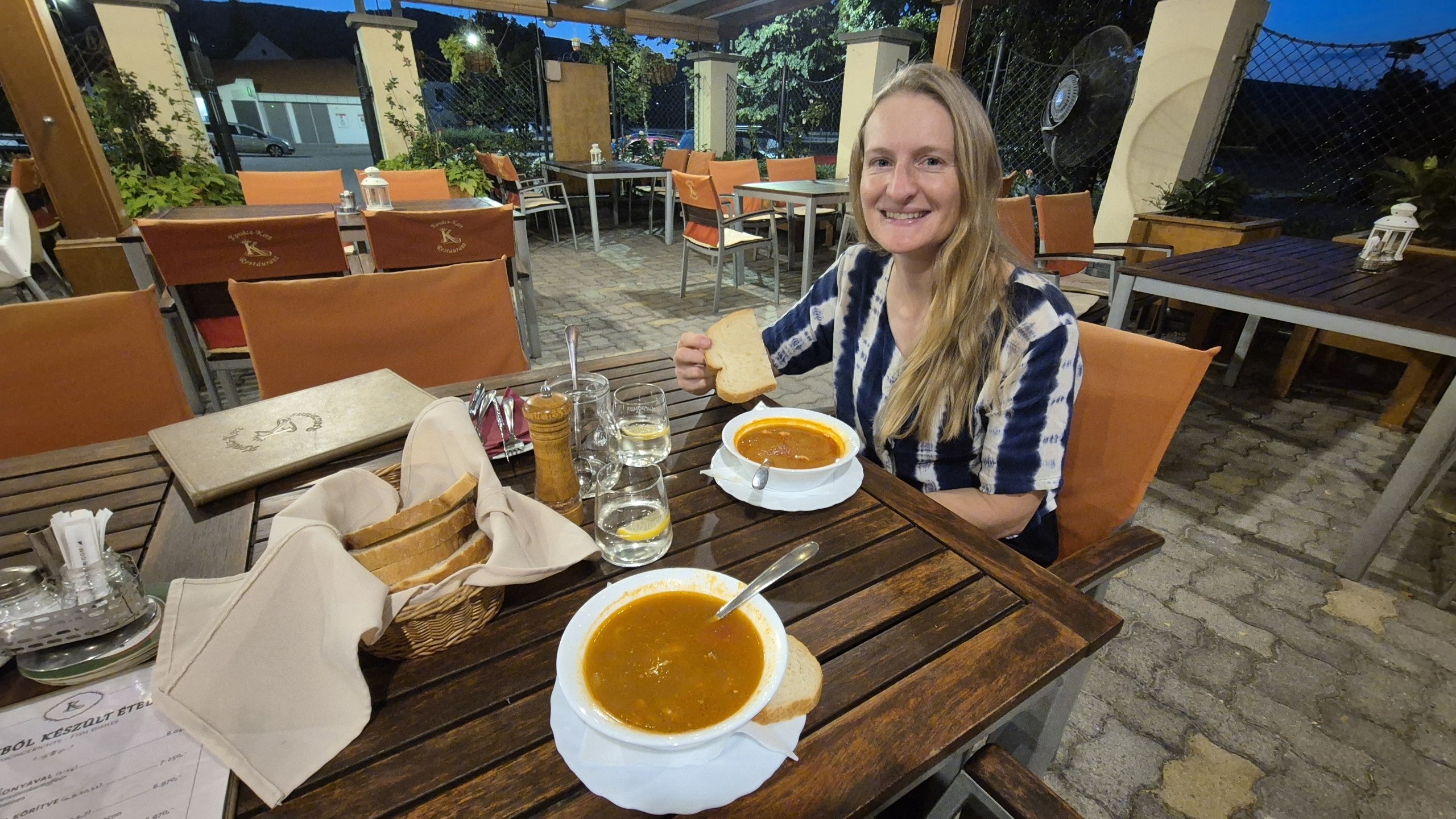 Caro sitting at an outdoor restaurant with two bowls of Hungarian soup