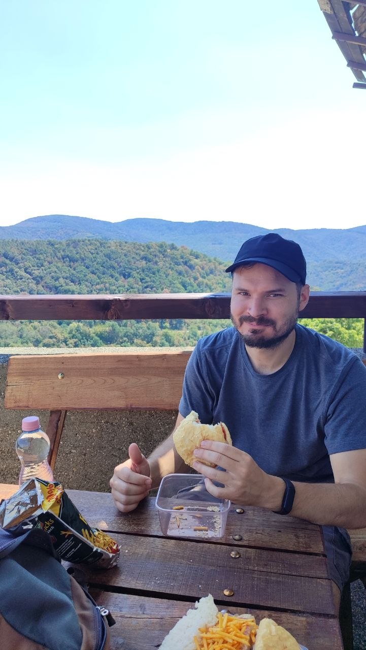 Hugo eating a cheese and salami bun at a picnic table above Visegrád