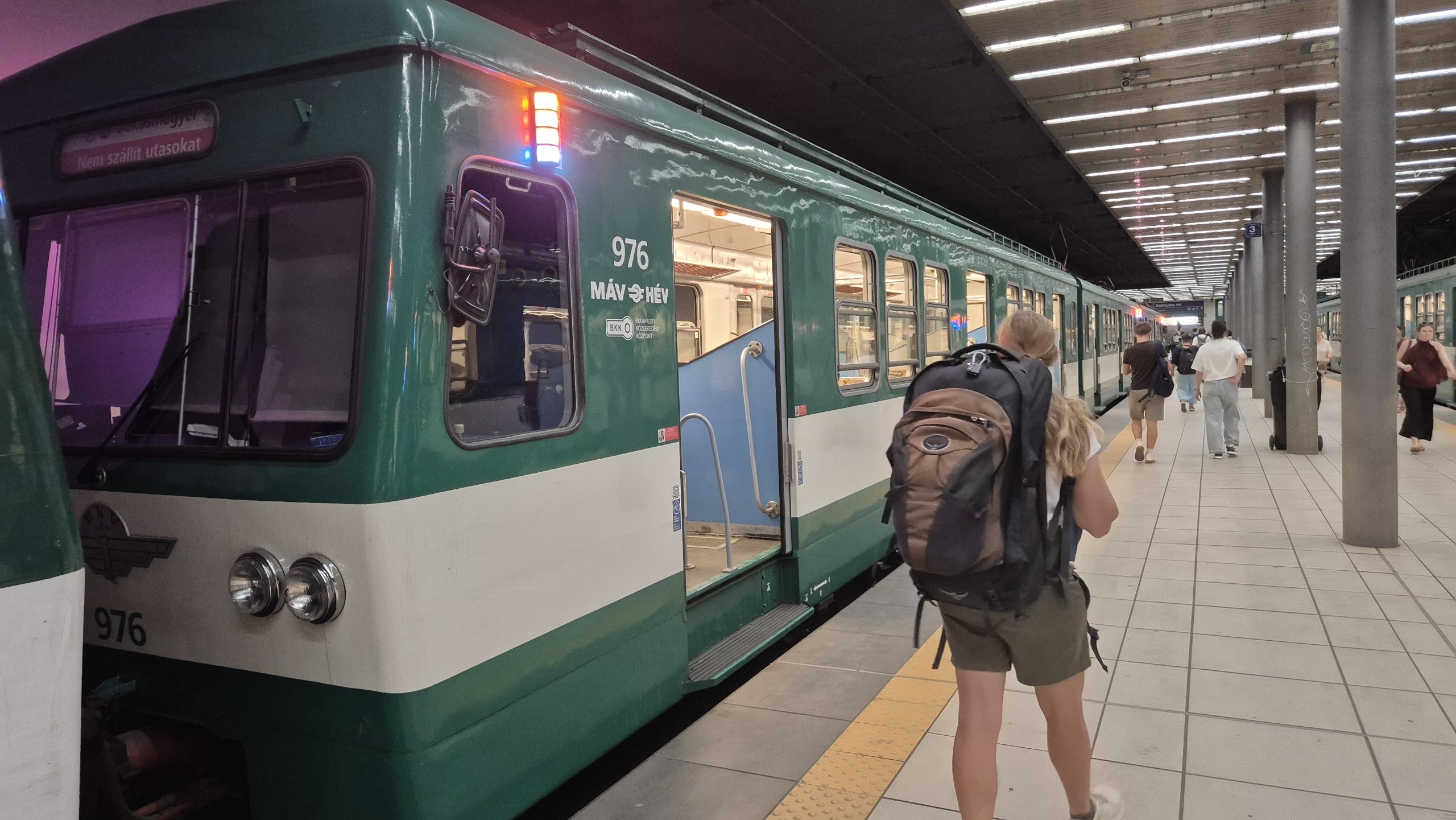 Caro carrying both backpacks beside the green H5 suburban train
