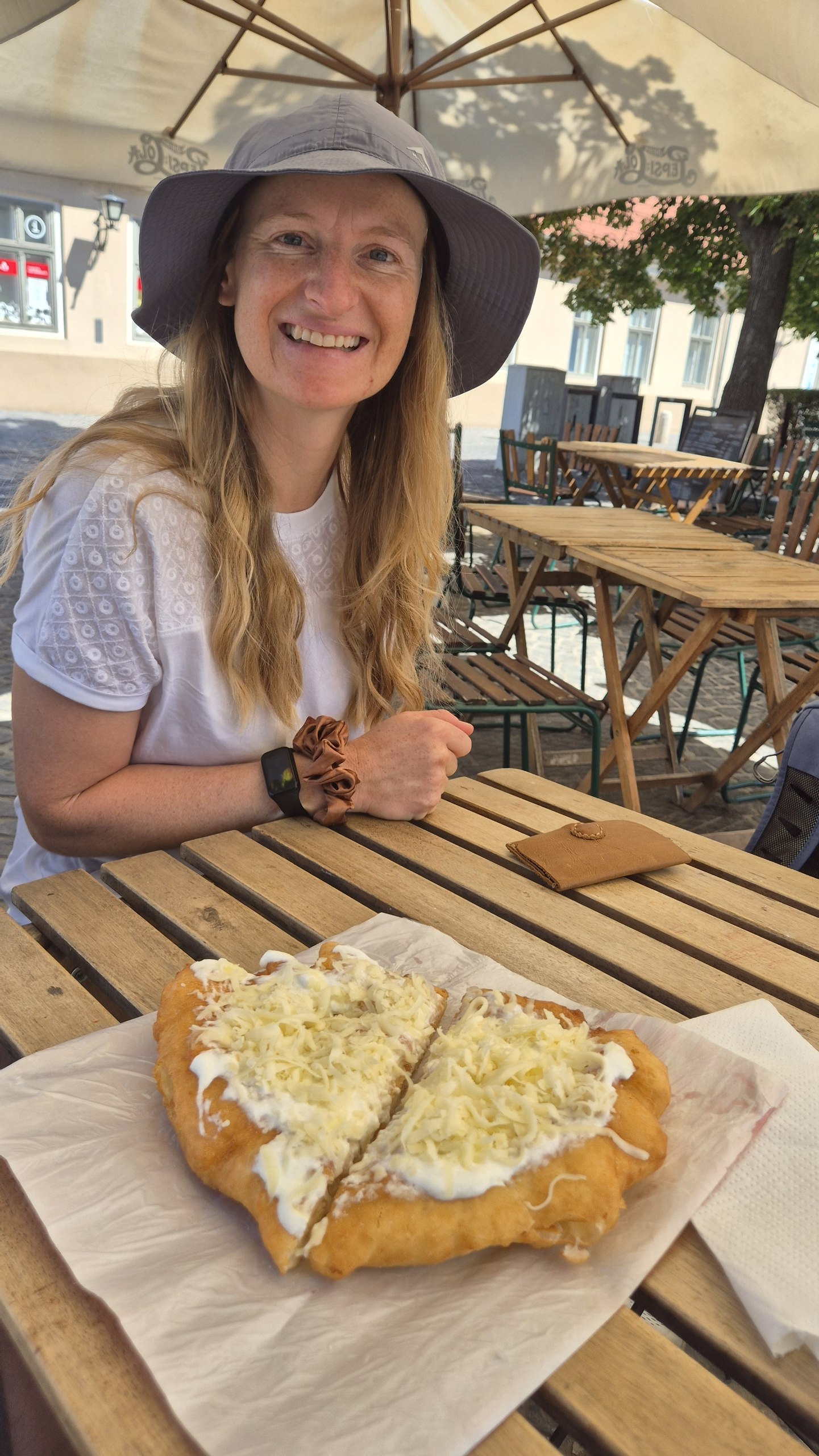 Caro smiling over a garlic, sour-cream and cheese lángos at an outdoor table in Szentendre