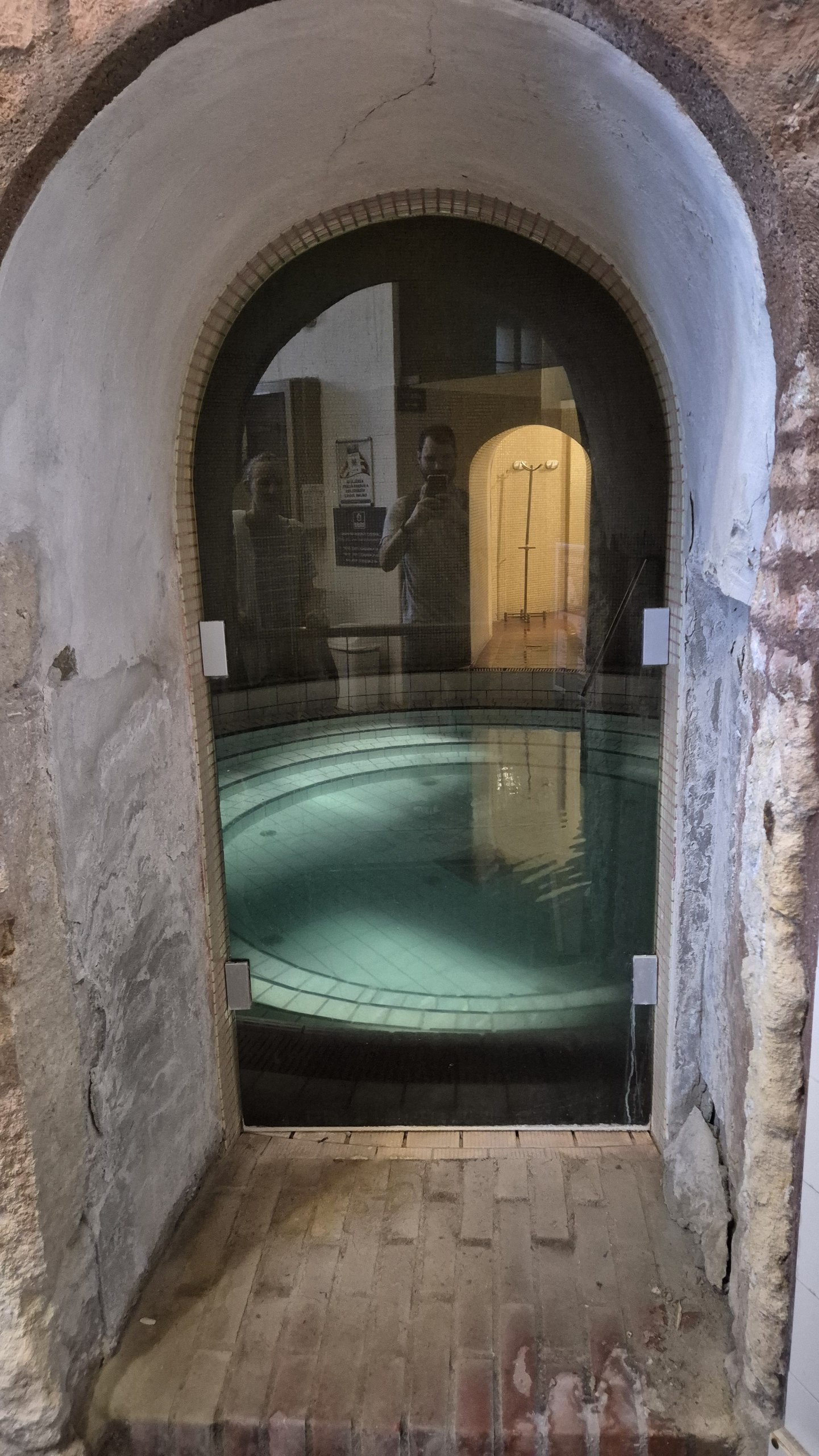 A small round thermal pool visible through an arched glass door at Lukács Baths