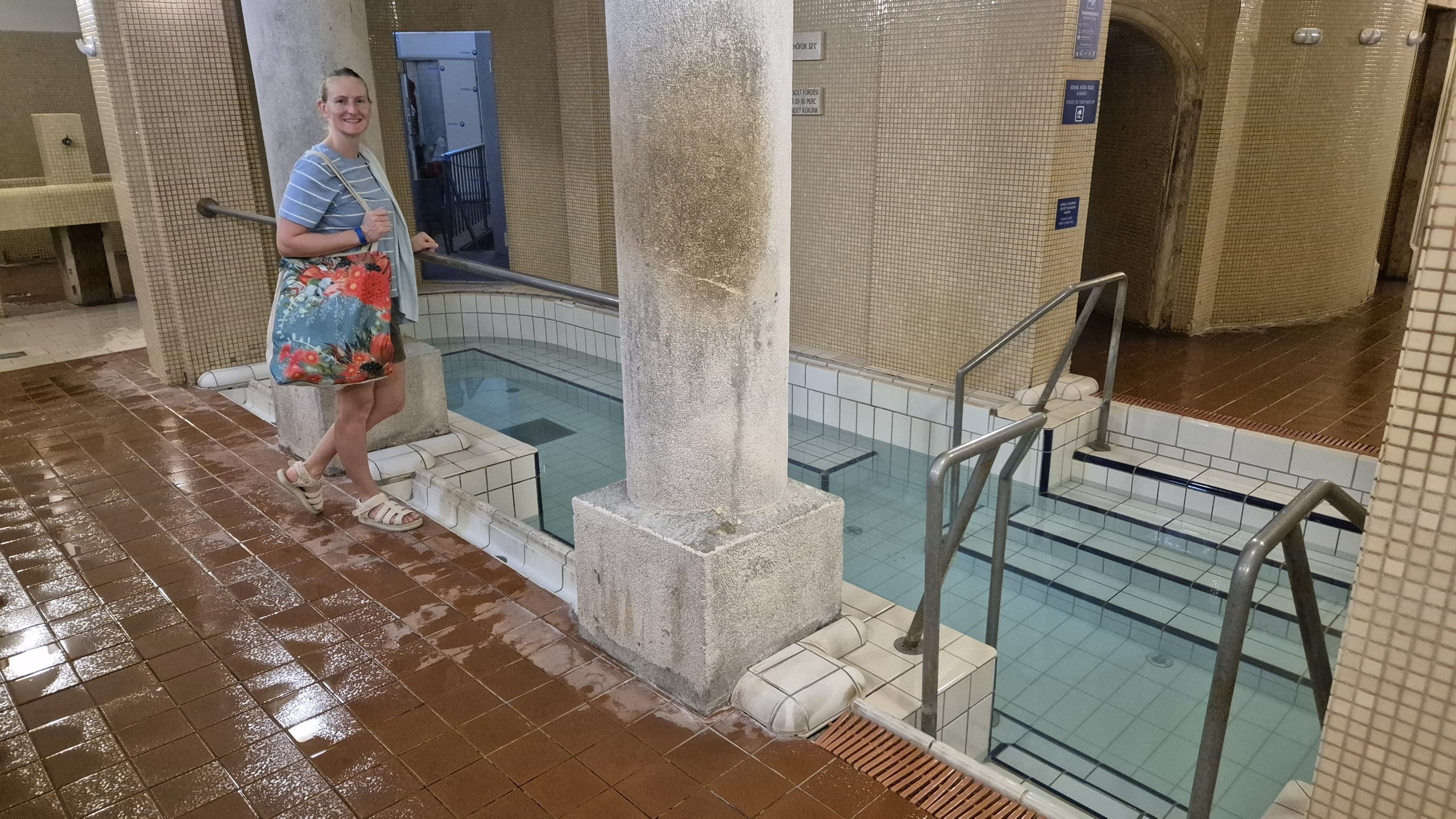 Caro standing beside the tiled indoor thermal pools at Lukács Baths