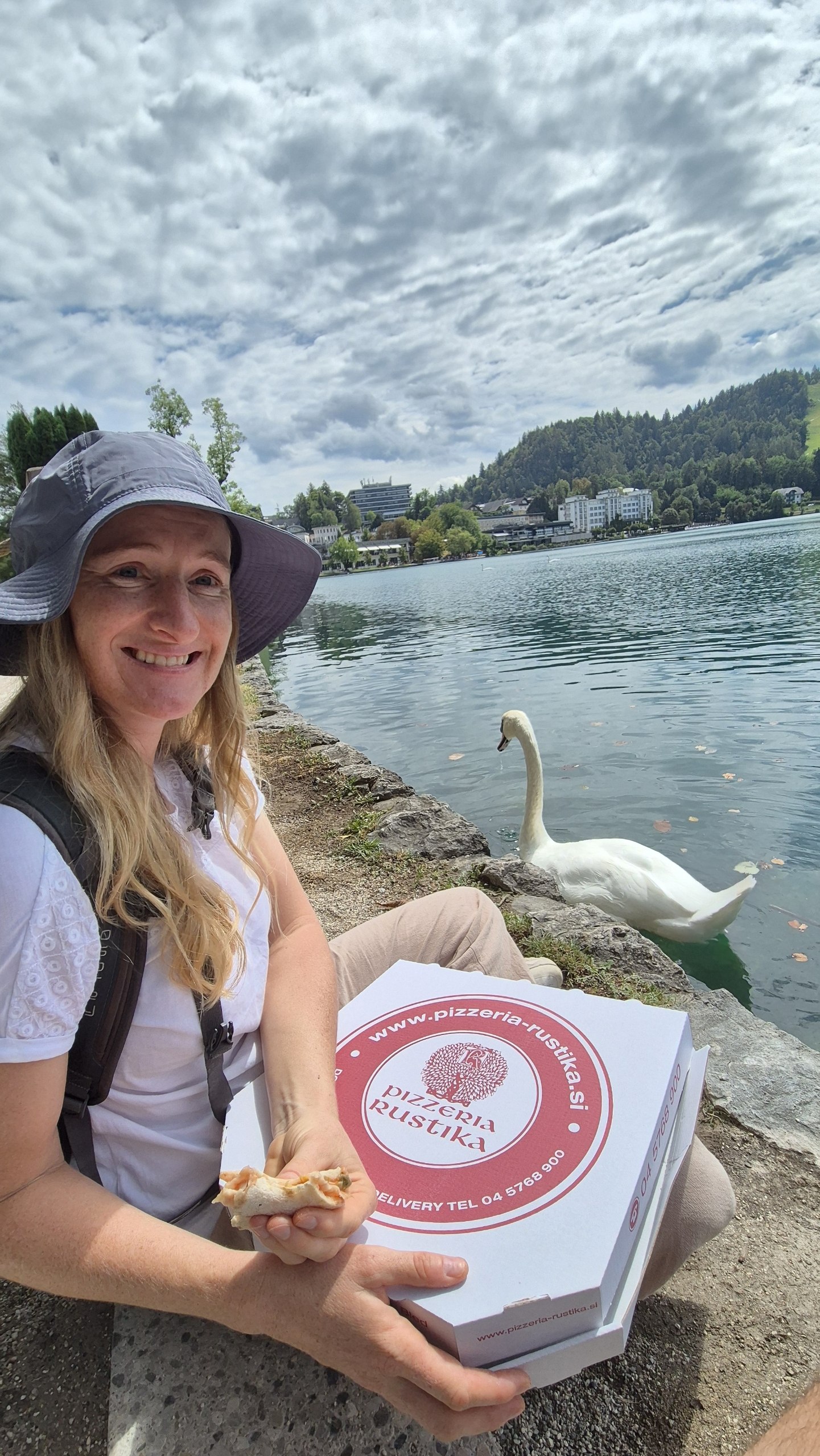 Caro eating pizza beside a swan at Lake Bled