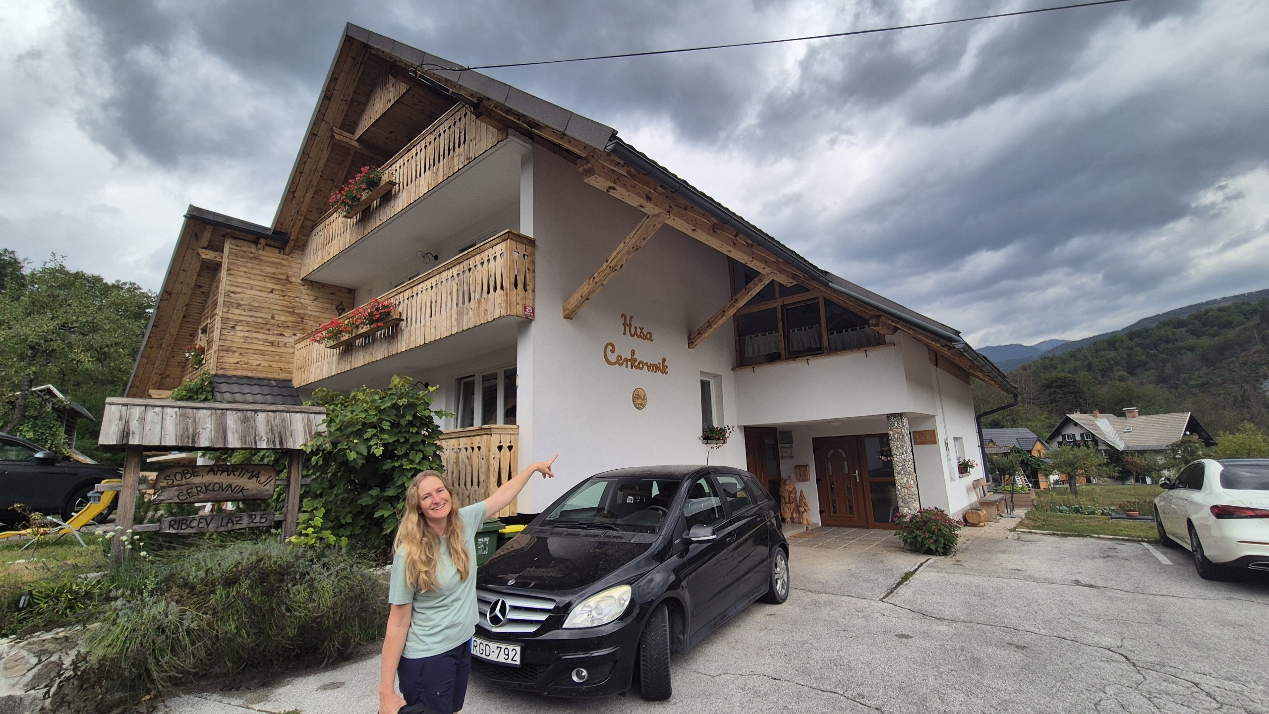 Caro pointing to the apartment building in Ribcev Laz beneath storm clouds