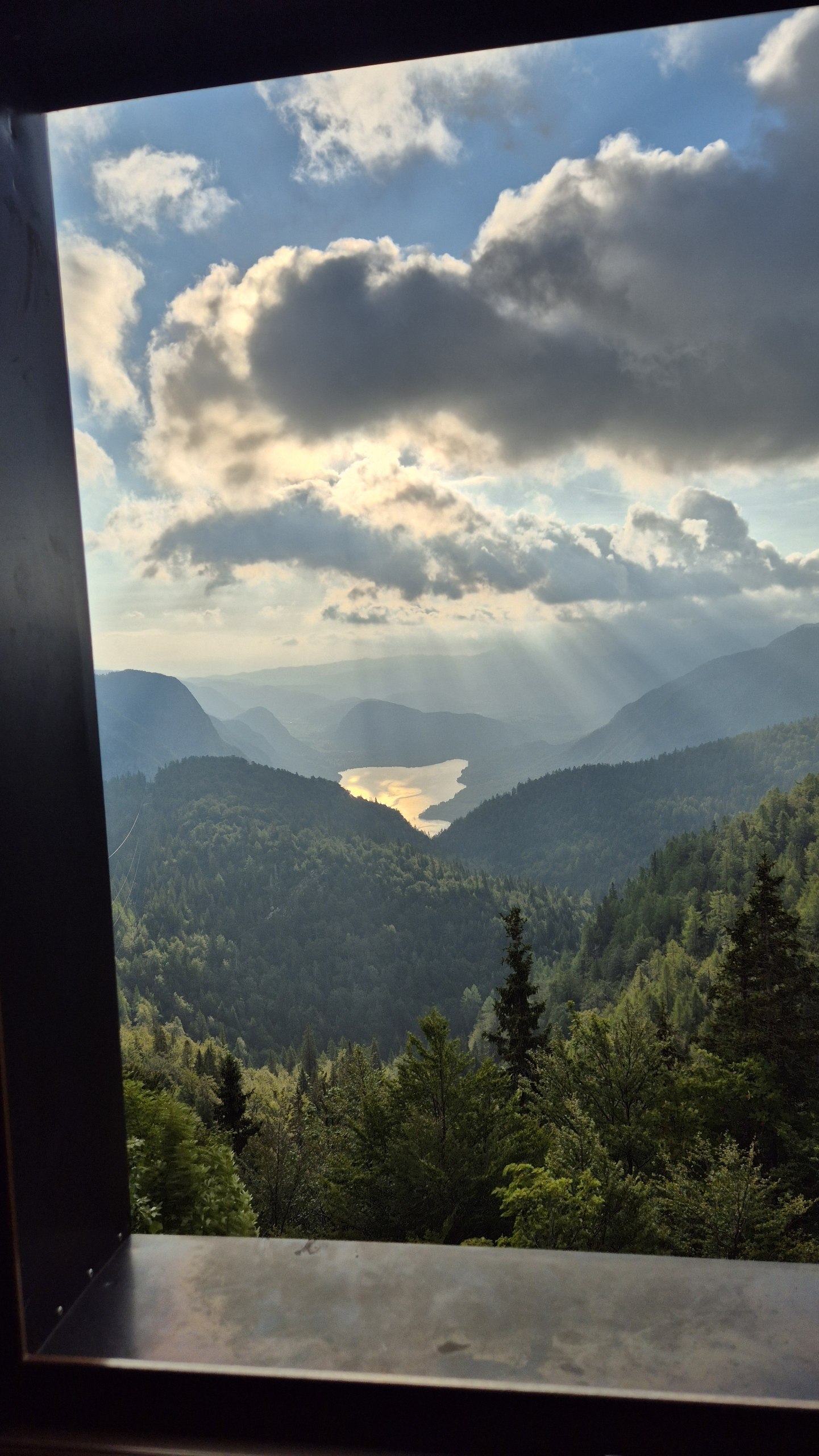 Lake Bohinj glowing in the distance beneath clouds, seen from Dom na Komni