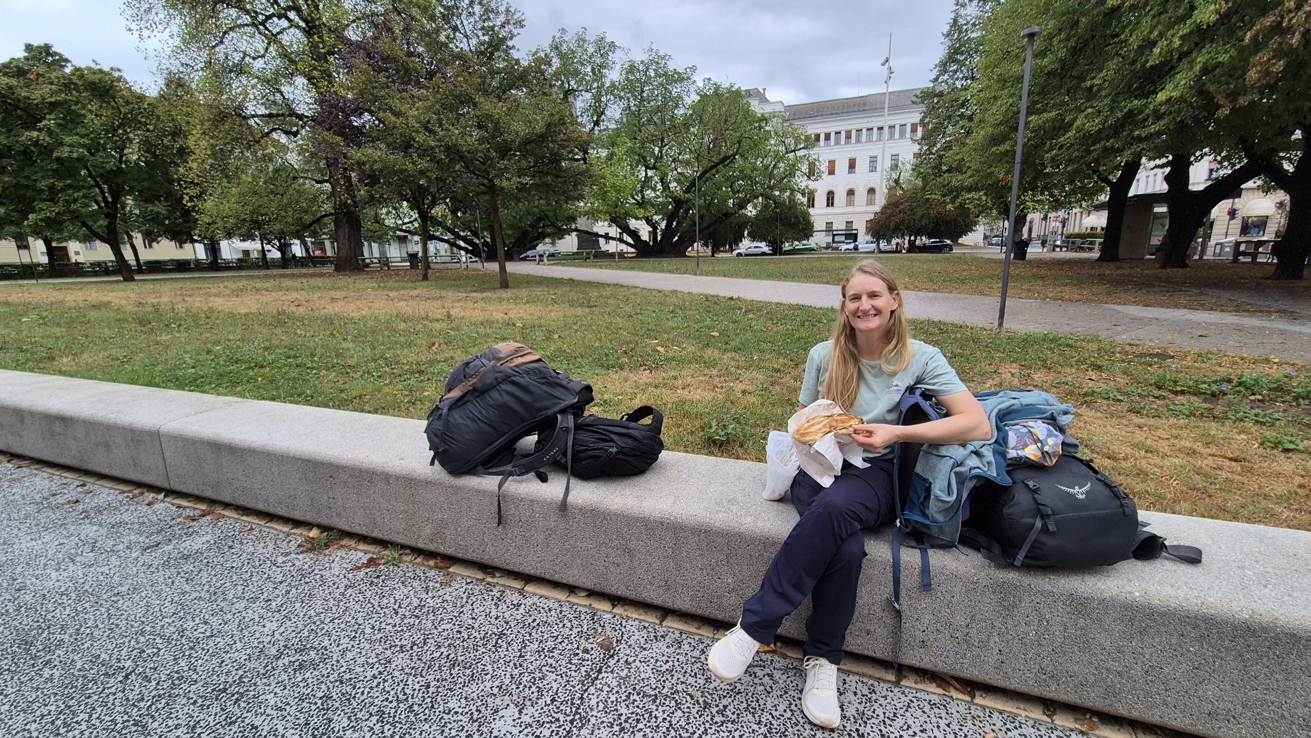 Caro eating an enormous burek in a Ljubljana park beside our luggage