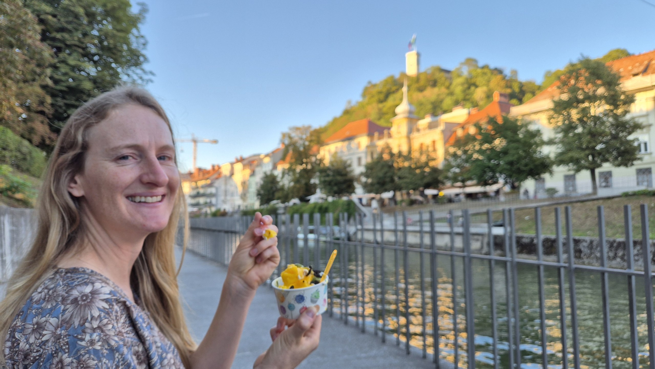 Caro eating frozen yoghurt beside the Ljubljanica with the castle behind her