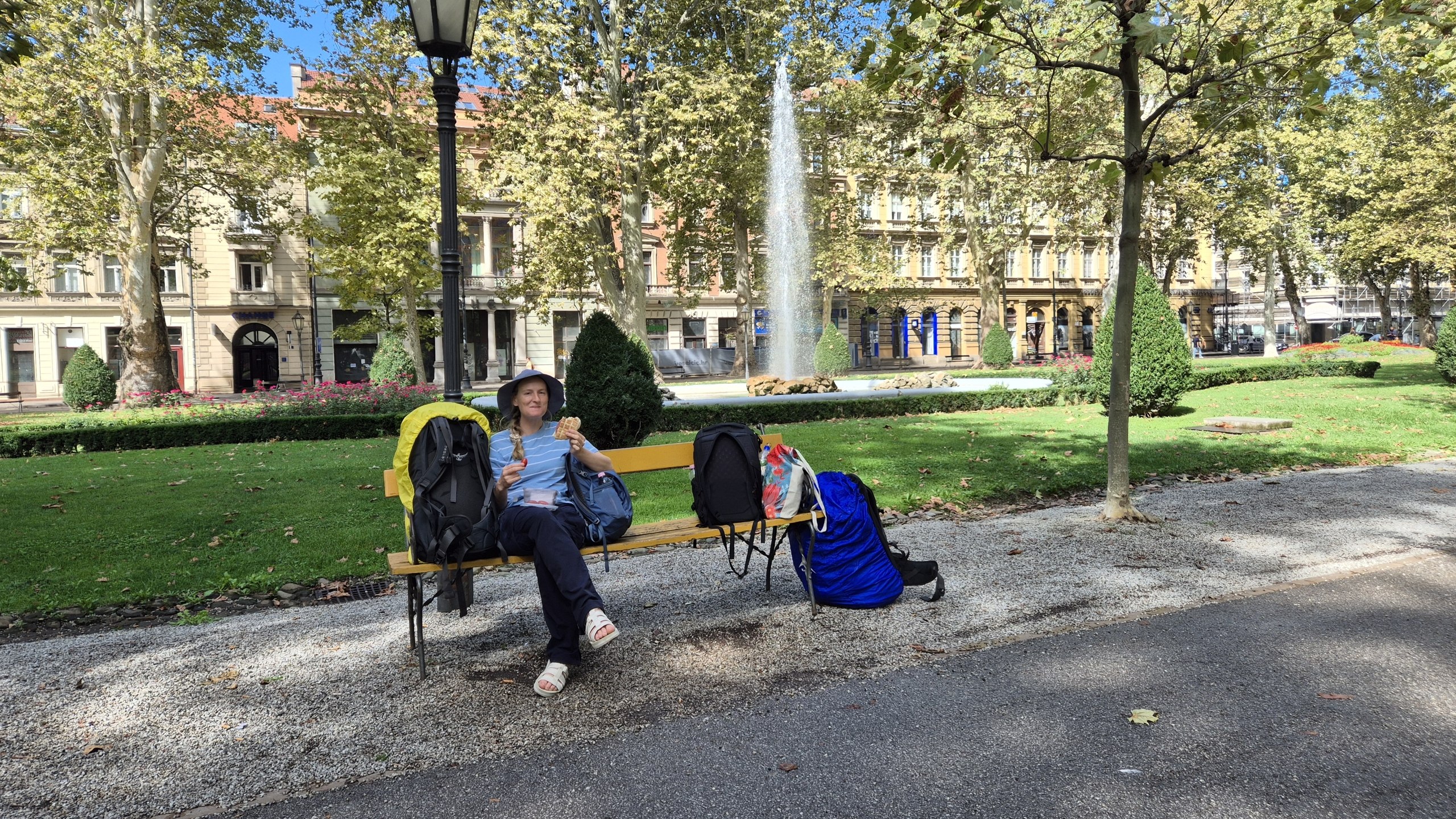 Caro eating a sandwich beside our luggage in Zrinjevac park Zagreb