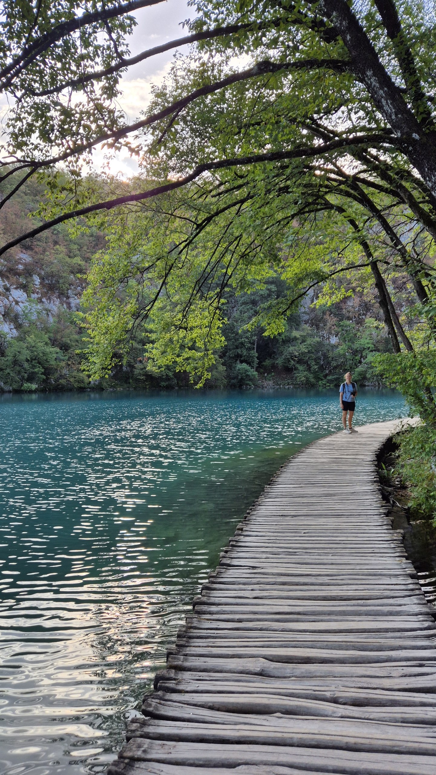 Caro on a wooden boardwalk beside a turquoise Plitvice lake