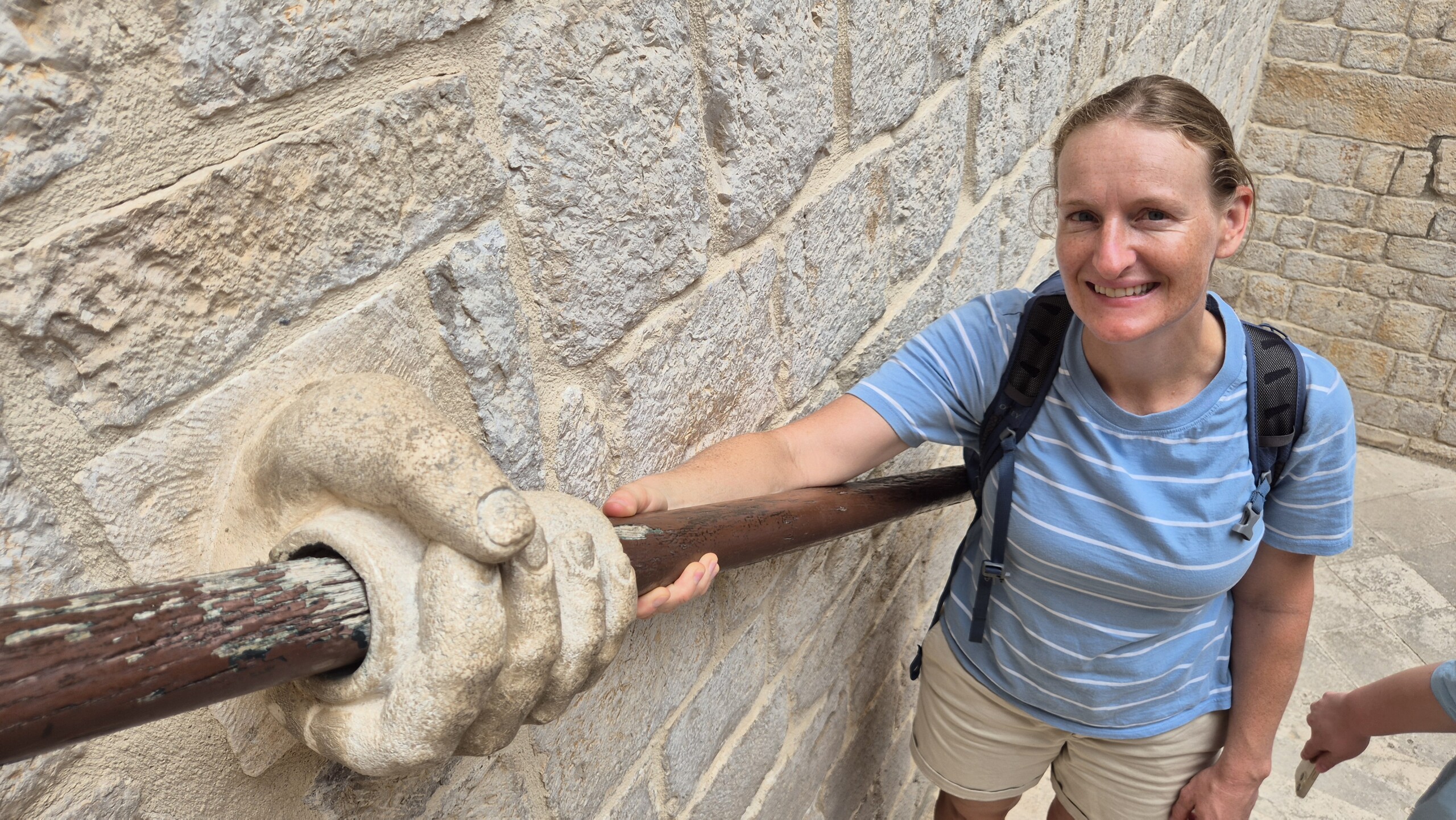 20260911_125716 Caro beside a carved stone hand and iron rail in Dubrovnik