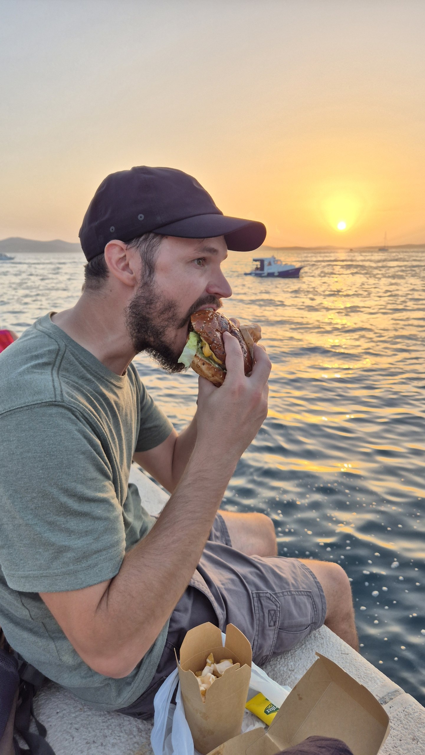 Hugo eating a burger beside the sea at sunset in Zadar