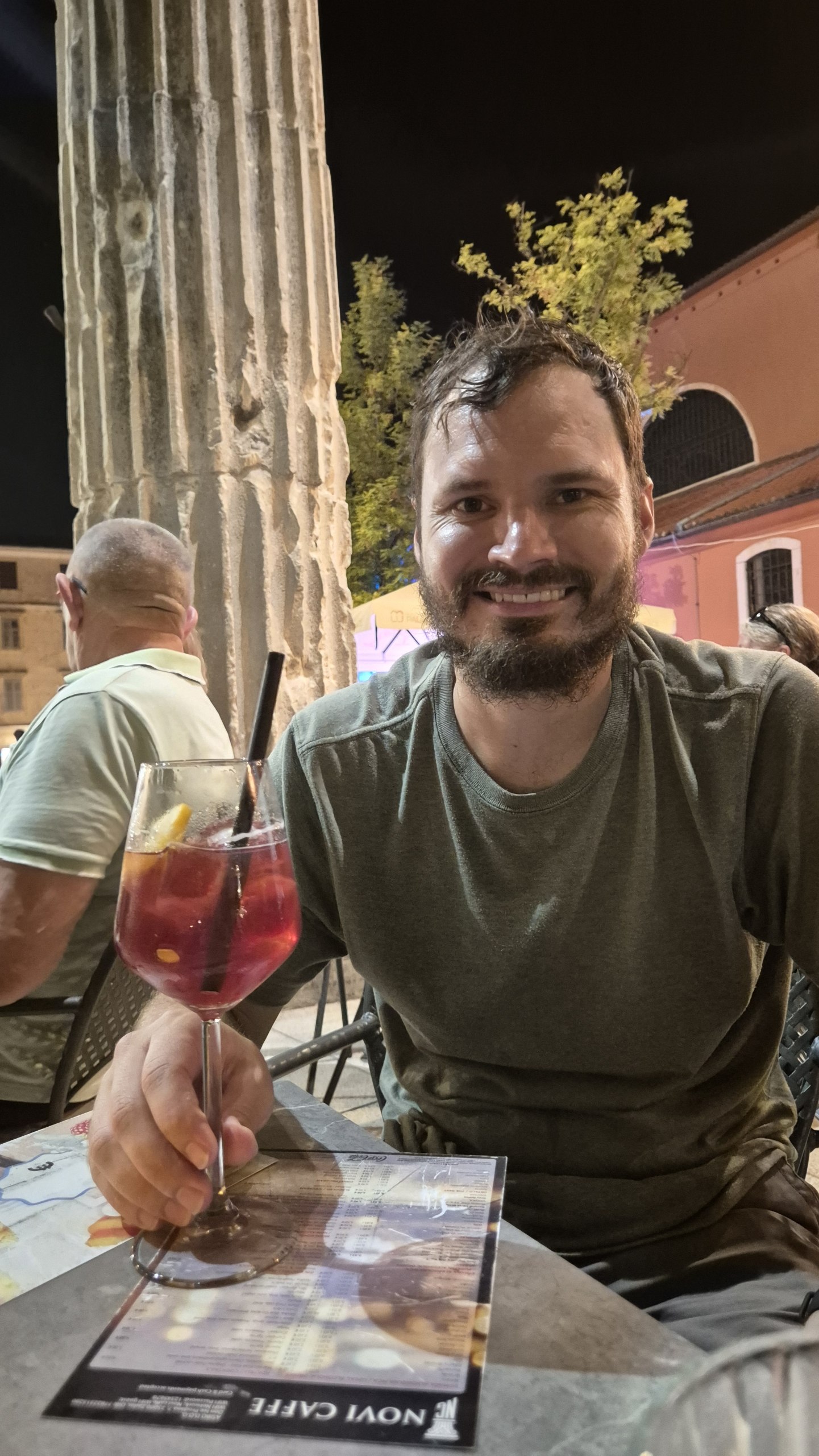 Hugo holding a red Maraschino cocktail at a cafe in Zadar