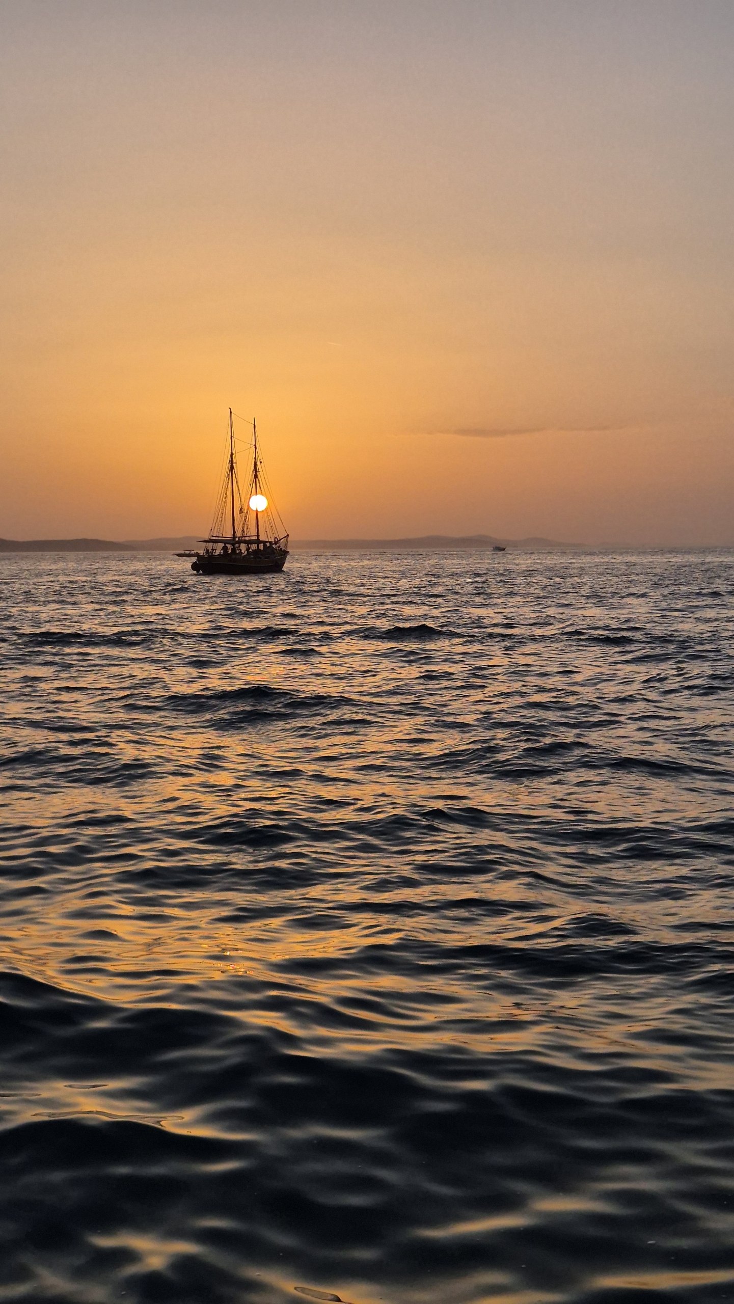 A sailboat silhouetted against the orange sunset off Zadar