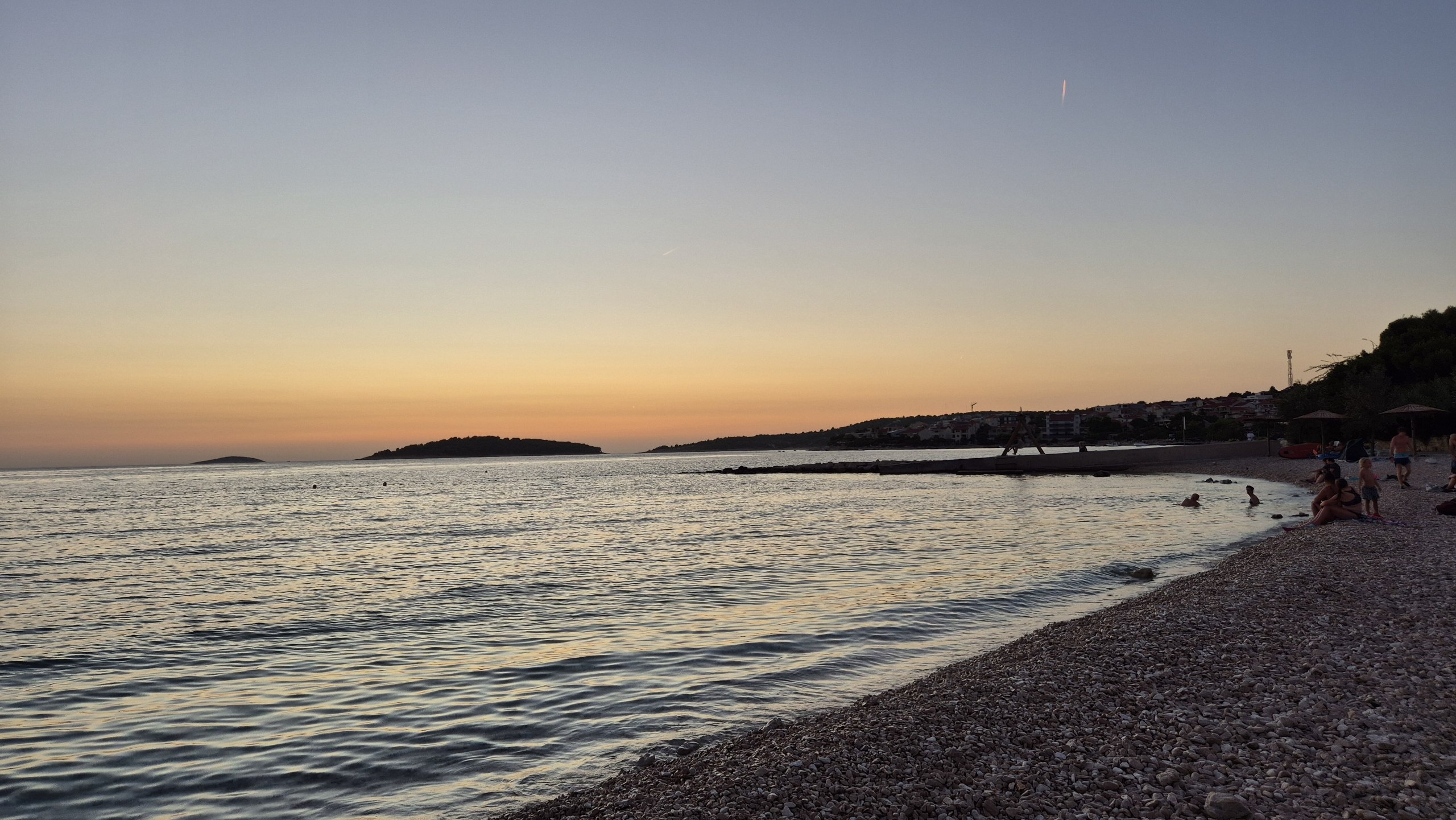 Calm water and a pebble beach in Rogoznica at sunset