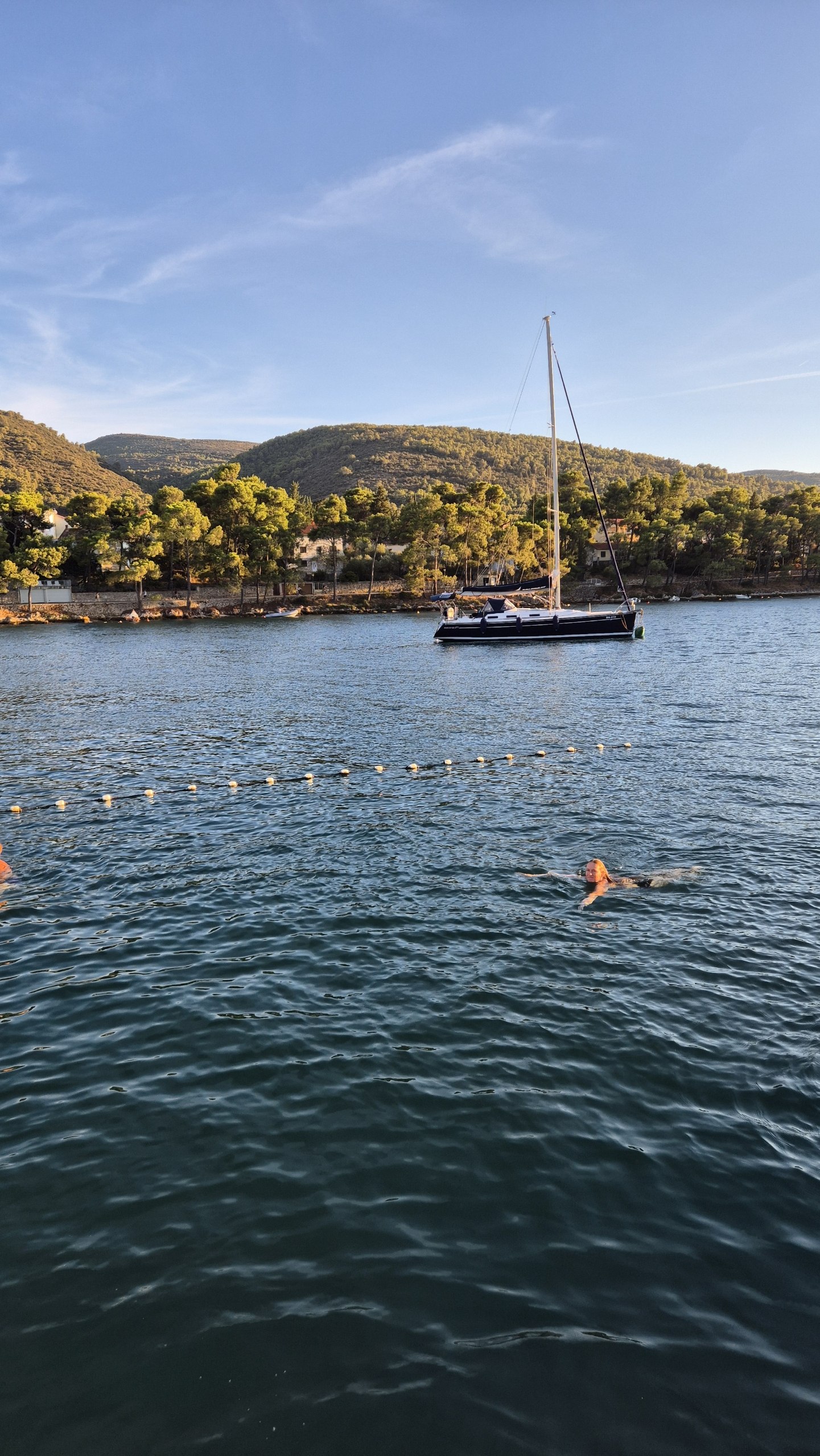 Caro swimming in Stari Grad harbour with a sailboat and wooded hills behind her