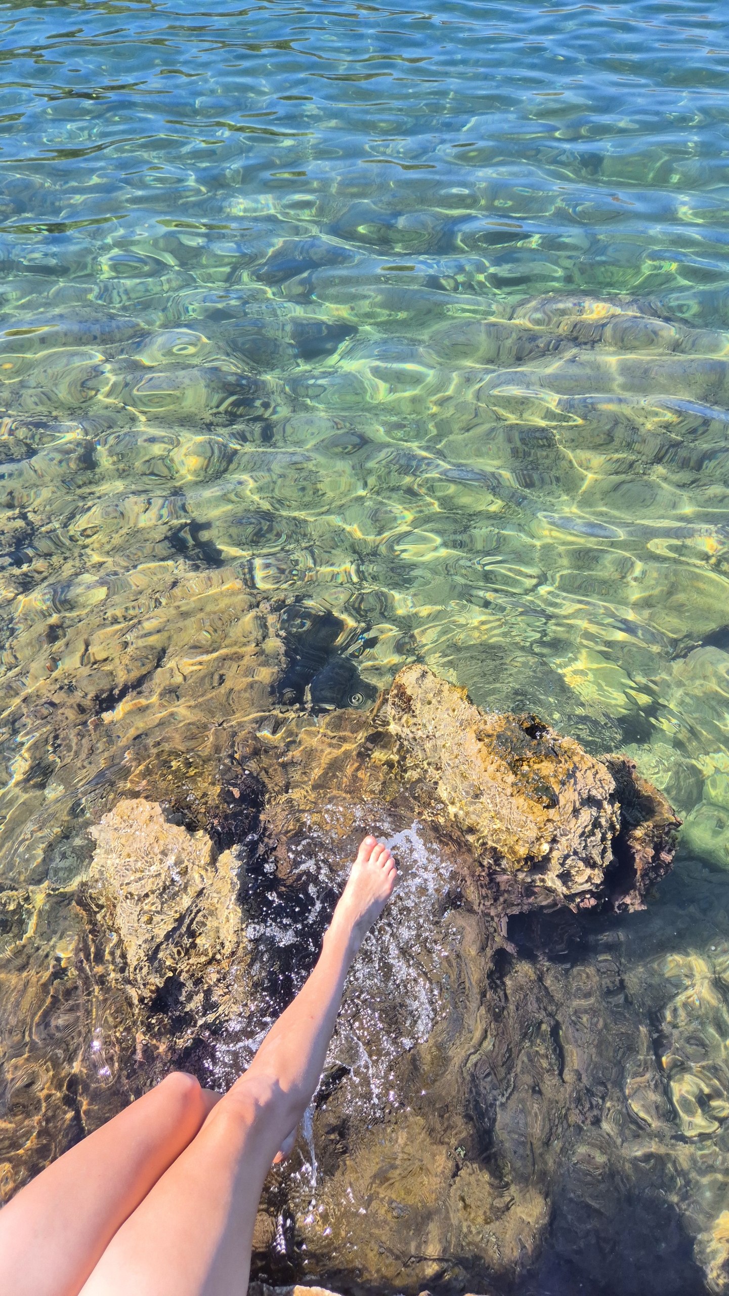 Caro's feet in the clear water among the rocks at Lanterna Beach