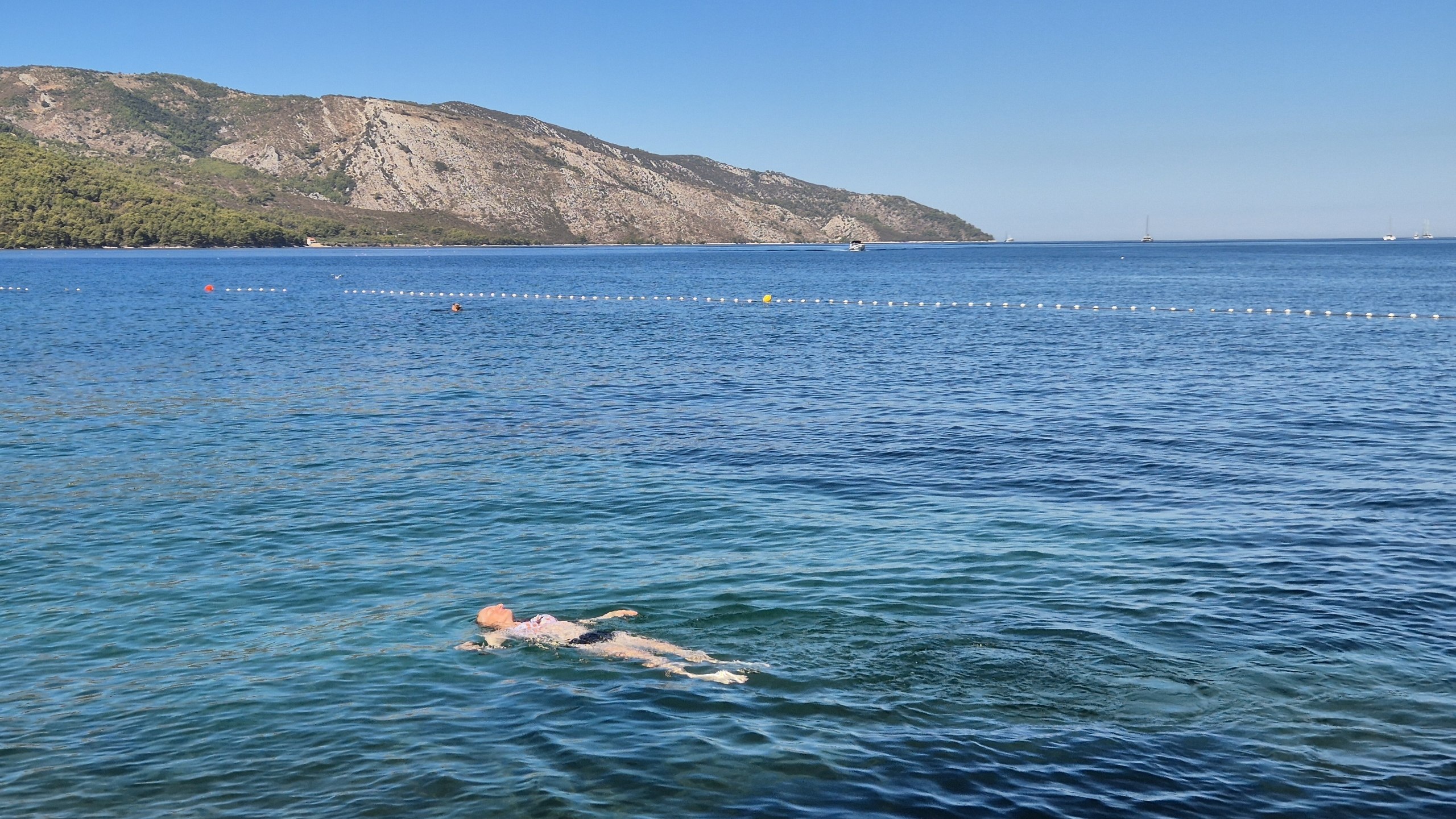 Caro floating in the clear sea at Lanterna Beach with the hills across the bay