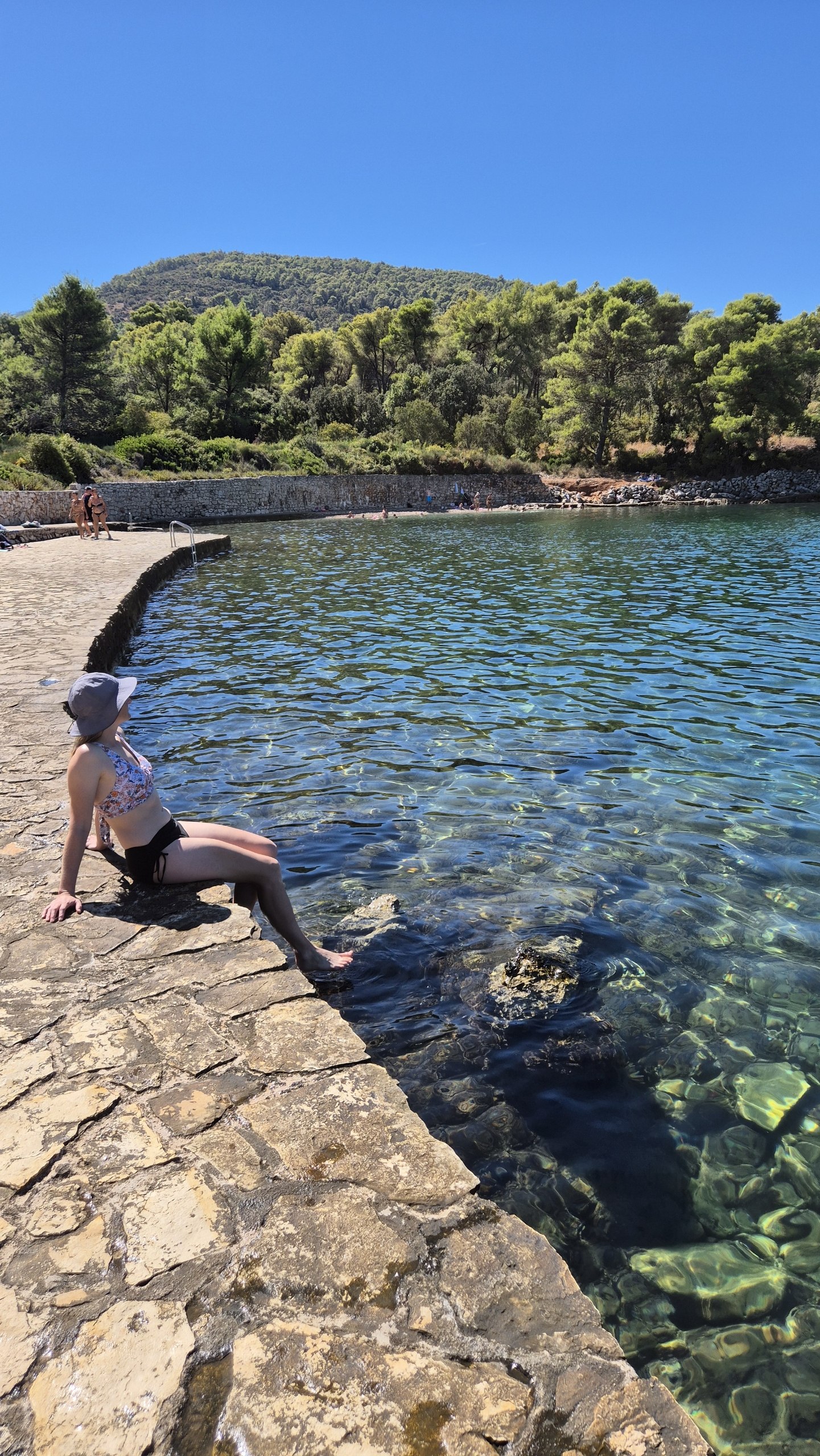 Caro sitting on the stone edge at Lanterna Beach