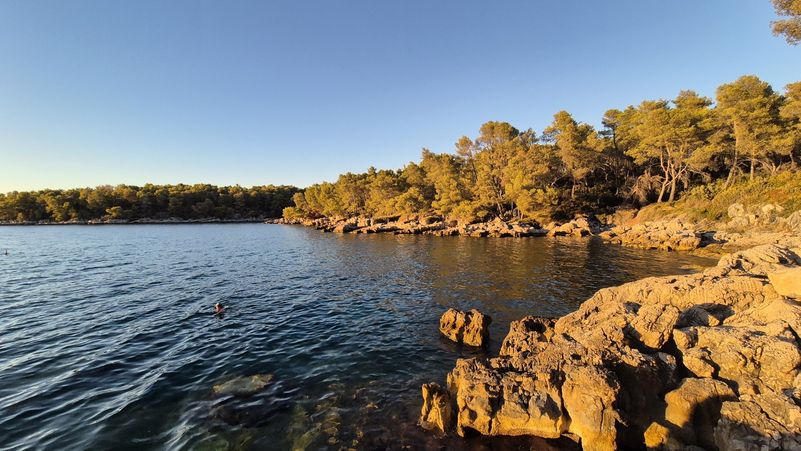 Swimmers in the calm bay at Uvala Zavala as the rocks glow in the evening sun