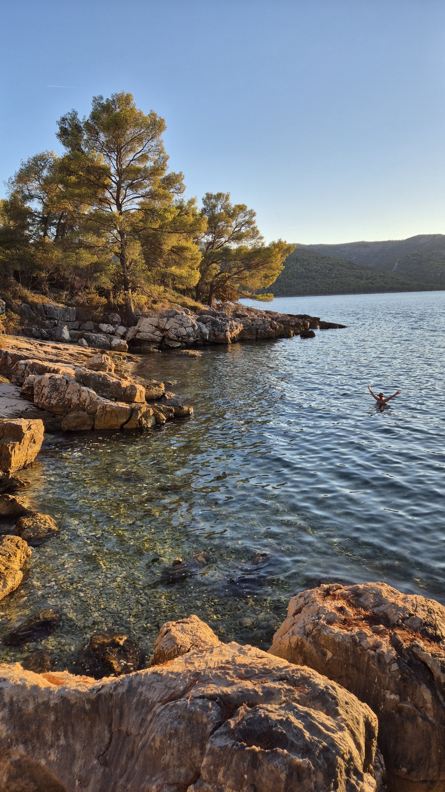 Rocky cove and swimmer in the golden light at Uvala Zavala