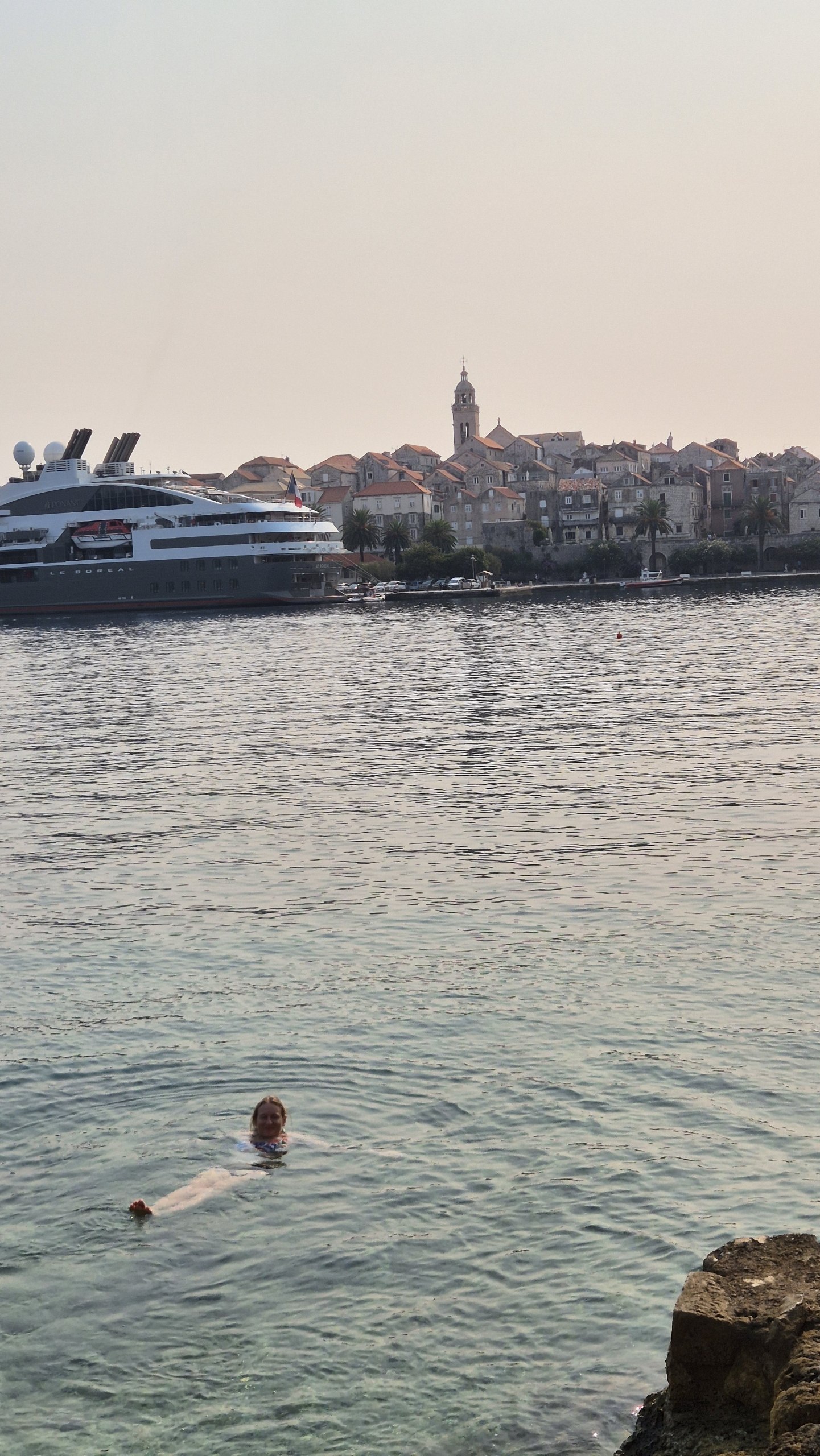 Caro swimming with Korcula old town and a large yacht behind her