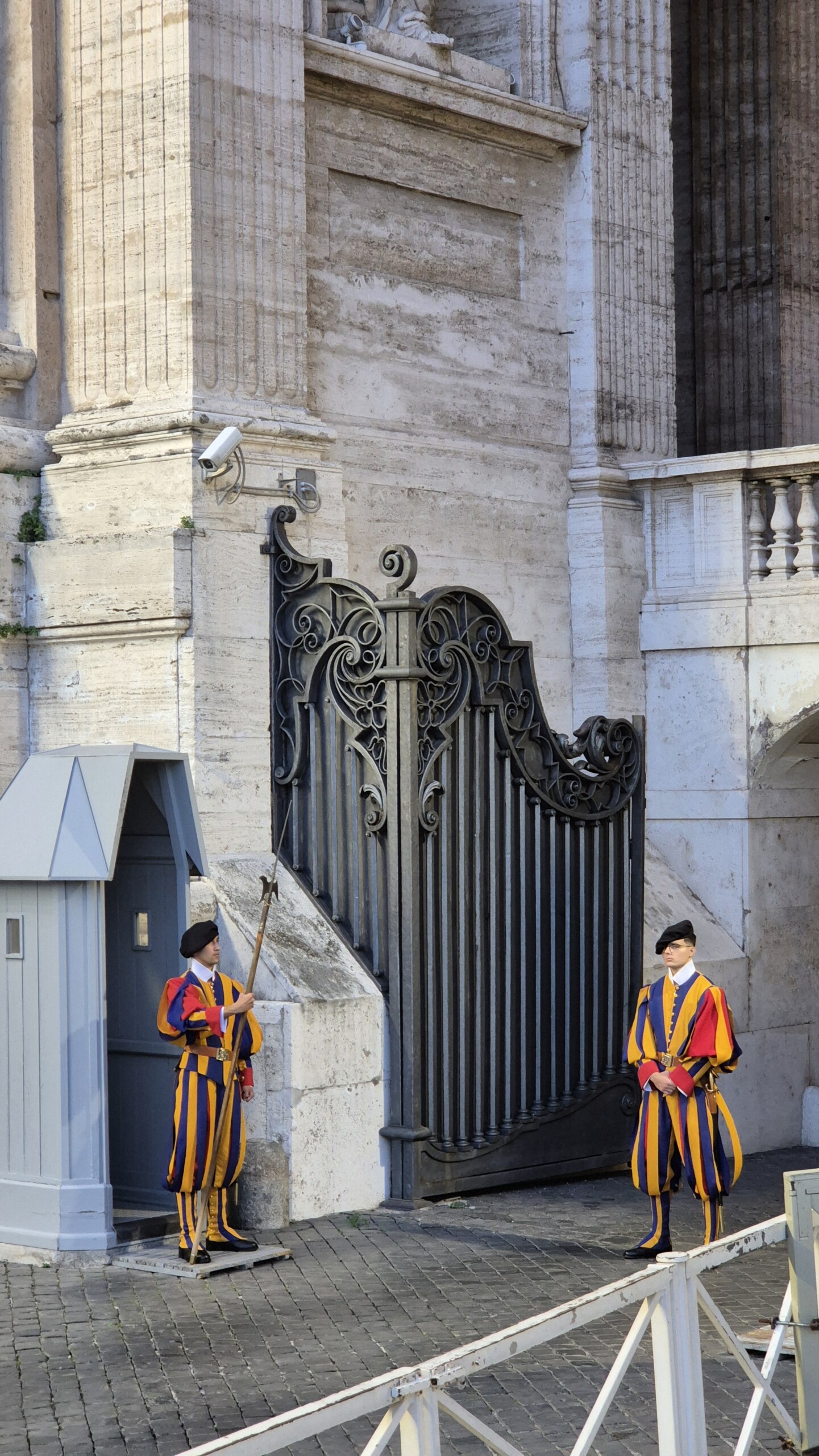 day64-swiss-guards Two Swiss Guards in striped uniforms on duty at a gate beside the basilica